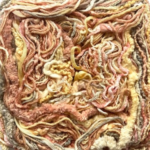 May include: Close-up of a ball of yarn in a mix of colors, including peach, cream, yellow, and gray. The yarn has a variety of textures, with some strands being thick and others thin. The yarn is tightly wound, creating a dense, textured ball.
