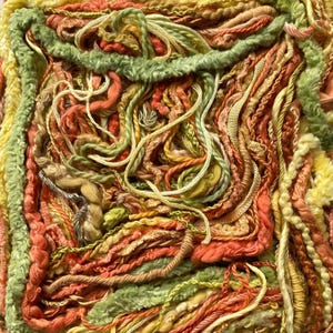 Puede incluir: Primer plano de una pieza de arte textil texturizada. La obra de arte presenta una variedad de hilos en tonos verdes, naranjas, amarillos y beige. Los hilos están dispuestos en un patrón tejido en capas, creando una superficie táctil y visualmente rica.
