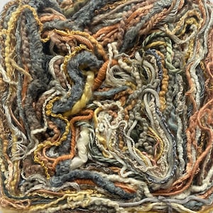 May include: Close-up of a textured yarn bundle in a square format. The yarn features a mix of colors, including gray, orange, yellow, and cream. The strands are thick and varied, creating a tactile and visually interesting surface. Ideal for fiber art projects.