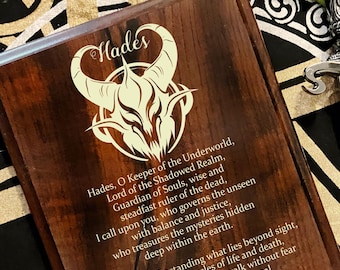 May include: A rectangular dark brown wooden plaque featuring a laser-engraved horned skull emblem and the text "Hades" followed by a prayer to the deity. The plaque is positioned next to a silver-toned metal dagger with an ornate handle.