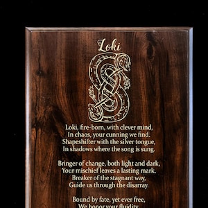 May include: A wooden plaque with a gold inscription about Loki, a Norse god. The inscription includes a poem about Loki's cunning and power. The plaque features a stylized image of a serpent.