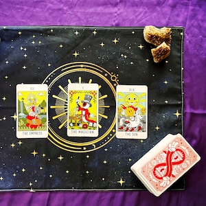 May include: Three tarot cards laid out on a black and gold tarot cloth with a starry pattern. The cards are "The Empress", "The Magician", and "The Sun".
