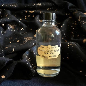 May include: A clear glass bottle with a black cap, containing a liquid. The bottle has a label that reads "Apr. 8, 2024 Total Solar Eclipse Water New Moon".