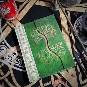 May include: A green journal with a gold tree design and a decorative border. The journal is closed and lying on a black and gold patterned surface.