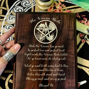 May include: A wooden plaque with a pentagram and the Wiccan Rede inscribed in gold lettering. The text reads: "Bide the Wiccan Law ye must, In perfect love and perfect trust. Eight words the Wiccan Rede fulfill: An' ye harm none, do what ye will. What ye send forth comes back to thee So ever mind the law of three. Follow this with mind and heart, Merry ye meet, and merry ye part. Blessed Be"