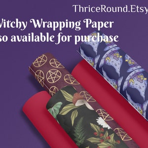 Puede incluir: Tres rollos de papel de regalo con diferentes dise&ntilde;os. El primer rollo tiene un fondo rojo oscuro con pentagramas dorados. El segundo rollo tiene un fondo verde oscuro con un patr&oacute;n floral. El tercer rollo tiene un fondo azul oscuro con un patr&oacute;n de sombreros de bruja. El texto "Witchy Wrapping Paper" y "Also available for purchase" es visible en la parte superior de la imagen.