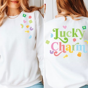 May include: White sweatshirt with a rainbow and green shamrock design on the front and the text "Lucky Charm" on the back.
