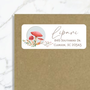 Pode incluir: Um rótulo de endereço de devolução branco com uma ilustração de aquarela de cogumelos vermelhos e folhas verdes. O texto "Lipani" está escrito em cursiva. O endereço é "846 Southbend Dr. Clemson, SC 20543".
