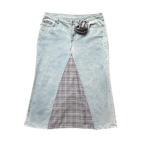 Könnte beinhalten: Hellblaue Jeansrock mit einem Karopaneel. Der Rock hat eine hohe Taille, einen ausgestellten Saum und eine dekorative Stoffblume an der Taille. Das Karopaneel ist grau, schwarz und weiß.