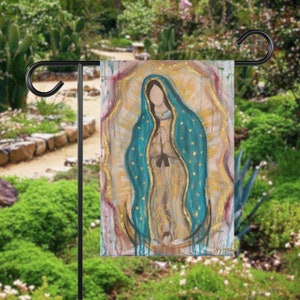 May include: A garden flag featuring a painting of the Virgin Mary, depicted in a blue and gold robe with a crown of stars. The background is a soft yellow with gold accents.