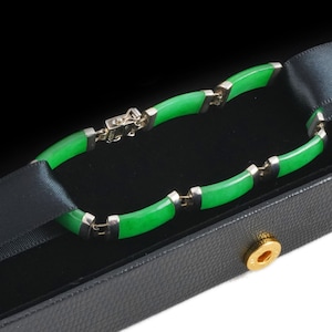 May include: A jade and silver bracelet with a clasp, displayed in a black velvet box with a gold accent.