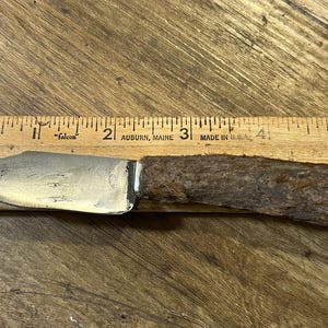 Op de afbeelding: Een klein, vintage mes met een zilveren lemmet en een getextureerde, bruine handgreep. Het mes ligt op een houten liniaal, het lemmet meet ongeveer 7.6 cm. De liniaal is gemarkeerd in inches.