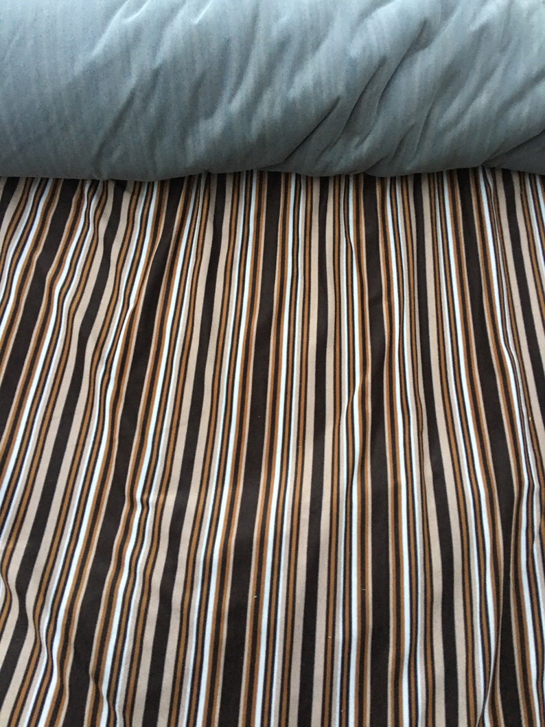 May include: A striped fabric with alternating brown, beige, and white stripes. The fabric is folded in half, with the top half folded over the bottom half.