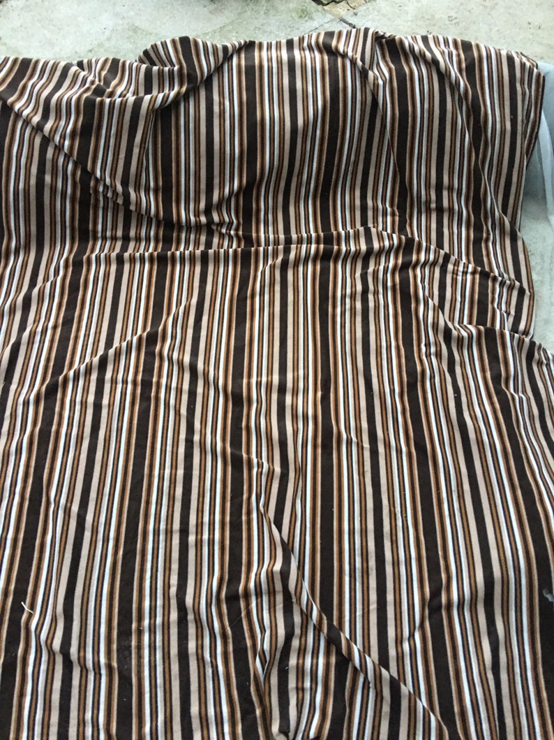 May include: A brown, white and beige striped blanket with a soft, fuzzy texture. The blanket is folded and draped over a surface.