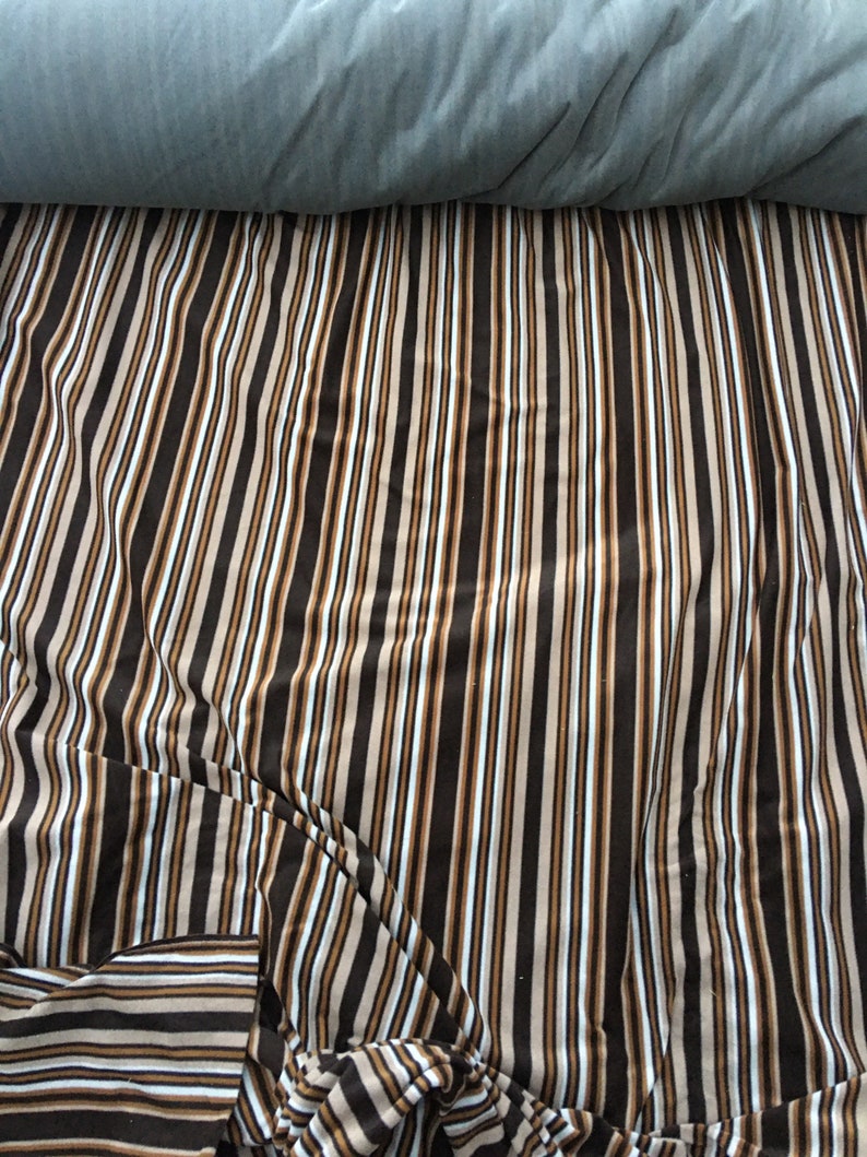 May include: A close-up of a striped fabric with brown, beige, and white stripes. The fabric is folded and creased, creating a textured look.