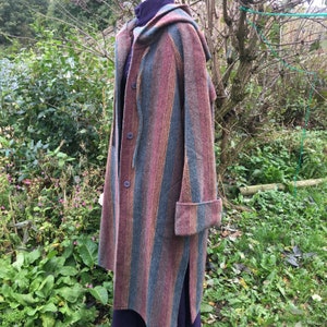 Peut inclure: Un long manteau à capuche rayé dans les tons bleu sarcelle, rose et marron. Le manteau a une fermeture à boutons et une poche sur le côté gauche.