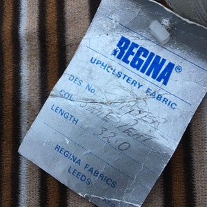 May include: A white tag with blue text that reads "REGINA UPHOLSTERY FABRIC" and has the following information: "DES. No. SRUE LEAT", "COL", "LENGTH 32.0", "REGINA FABRICS LEEDS", and "PT.O."