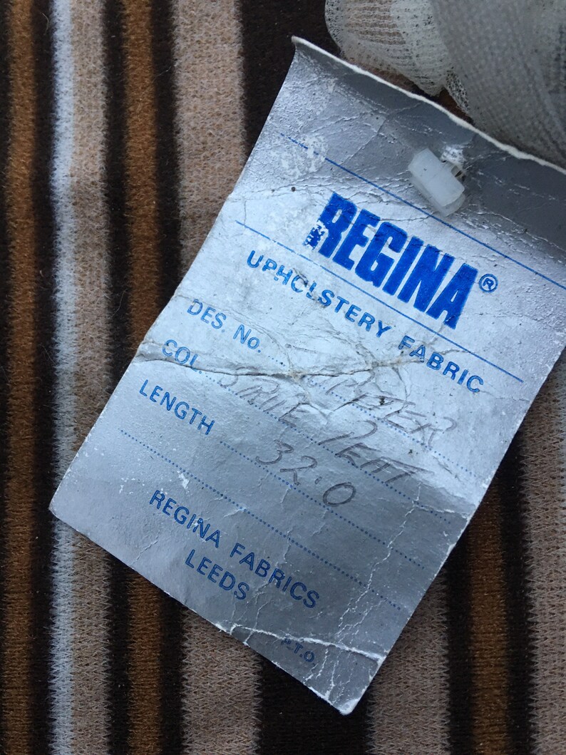 May include: A white tag with blue text that reads "REGINA UPHOLSTERY FABRIC" and has the following information: "DES. No. SRUE LEAT", "COL", "LENGTH 32.0", "REGINA FABRICS LEEDS", and "PT.O."