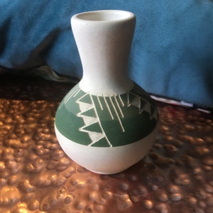 May include: A white ceramic vase with a green geometric design. The vase has a narrow neck and a rounded body.