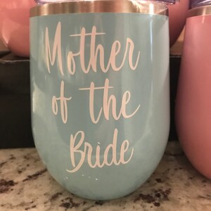 May include: A light blue stainless steel wine tumbler with a gold rim and the text "Mother of the Bride" in white lettering.