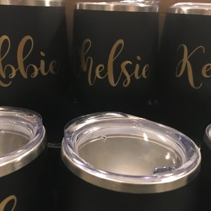 May include: Three black stainless steel tumblers with gold lettering. The tumblers are labeled "Abbie", "Kelsie", and "Kelli".