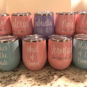 May include: Set of 9 stainless steel wine tumblers with various pastel colors and white text. The text includes "Bridesmaid", "Maid of Honor", "Mother of the Bride", "Mother of the Groom", and names.