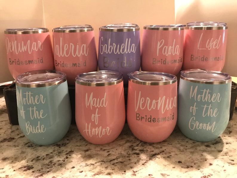 May include: Set of 9 stainless steel wine tumblers with various pastel colors and white text. The text includes "Bridesmaid", "Maid of Honor", "Mother of the Bride", "Mother of the Groom", and names.
