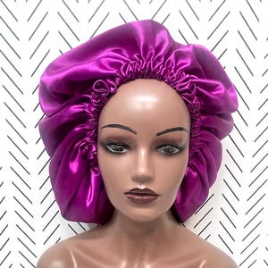 May include: A purple satin bonnet for sleeping or styling hair. The bonnet is gathered at the top and has a smooth, silky texture.