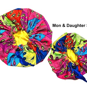 May include: A set of two colorful satin bonnets with a yellow lining and a blue drawstring. The bonnets are patterned with pink, blue, green, and yellow. The text "Mon & Daughter Set" is visible in the image.