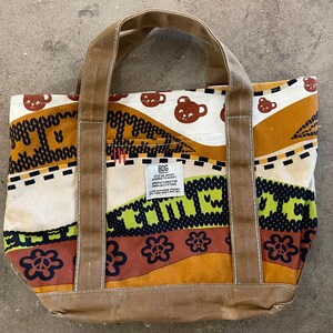 May include: A colorful tote bag with brown handles and a patterned design. The bag features a repeating pattern of brown bear faces, flowers, and geometric shapes in shades of brown, green, and cream. The bag has a label that says "BDG".
