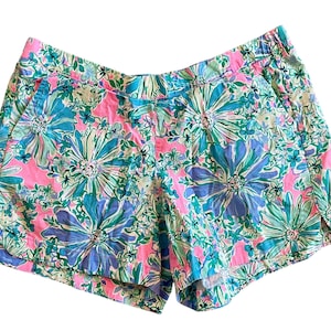 May include: Floral print shorts in pink, blue, and green. The shorts feature a vibrant pattern of large flowers and leaves. The shorts have pockets and an elastic waistband. The shorts are made of a lightweight fabric.
