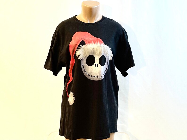 May include: Black t-shirt with a graphic of Jack Skellington from The Nightmare Before Christmas wearing a Santa hat.