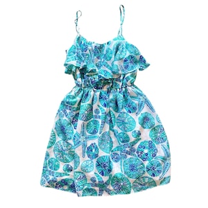 May include: A sleeveless dress with a white background and a pattern of blue and teal sea creatures. The dress has thin spaghetti straps, a ruffled neckline, and an elastic waist. The skirt is flared.