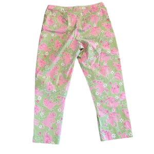 May include: Green pants with a pink bunny rabbit print. The pants have a relaxed fit and a cropped length.
