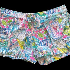May include: Blue and white patterned shorts with a pink and green watermelon print. The shorts have a ruffled hem and a drawstring waist.