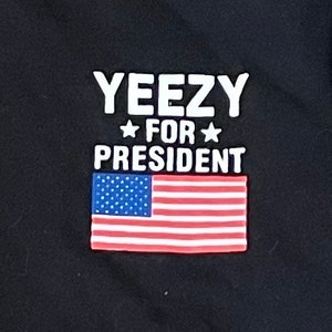 May include: Black t-shirt with white text that reads "Yeezy for President" and a red, white, and blue American flag.