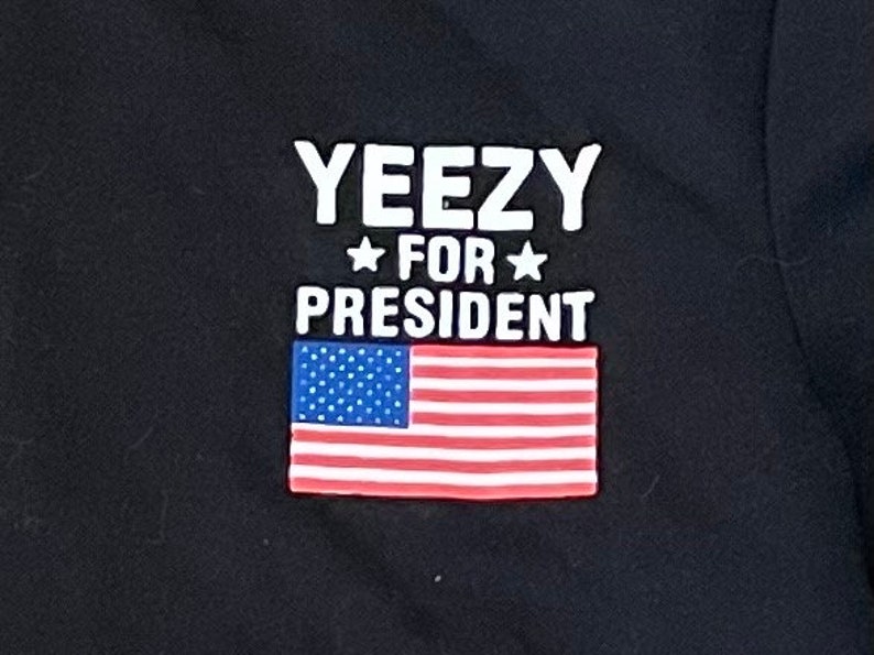 May include: Black t-shirt with white text that reads "Yeezy for President" and a red, white, and blue American flag.