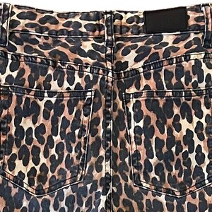 Op de afbeelding: Een paar bruine en zwarte jeans met luipaardprint en een achterzak. De jeans heeft een zwart leren patch op de achterkant van de tailleband.