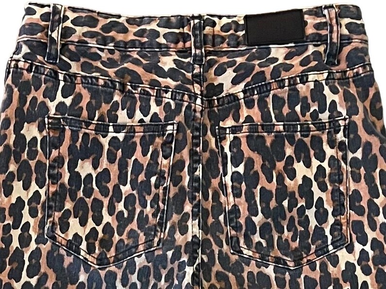 Op de afbeelding: Een paar bruine en zwarte jeans met luipaardprint en een achterzak. De jeans heeft een zwart leren patch op de achterkant van de tailleband.