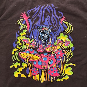 May include: A black t-shirt with a colorful graphic print of a wizard with a long beard surrounded by mushrooms. The text "MAGIC" is written in a stylized font above the wizard.