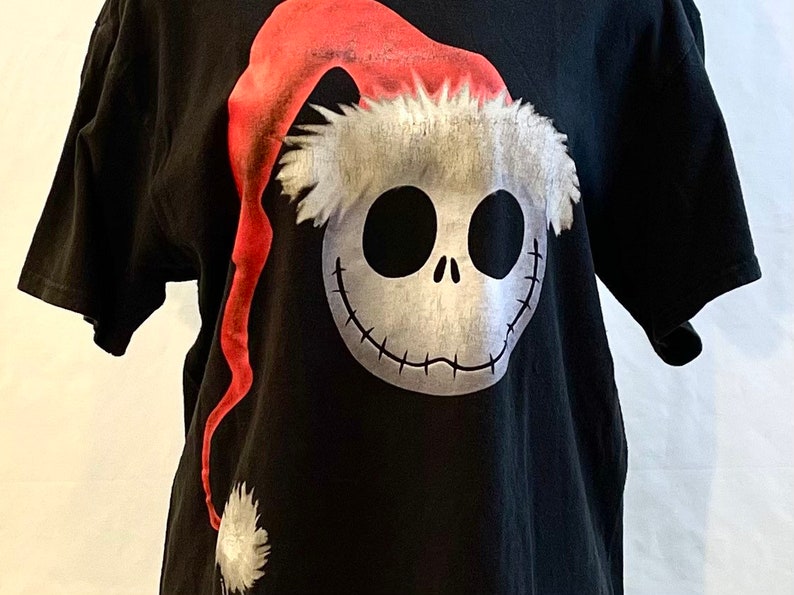 May include: Black t-shirt with a white and red graphic of Jack Skellington from The Nightmare Before Christmas wearing a Santa hat.