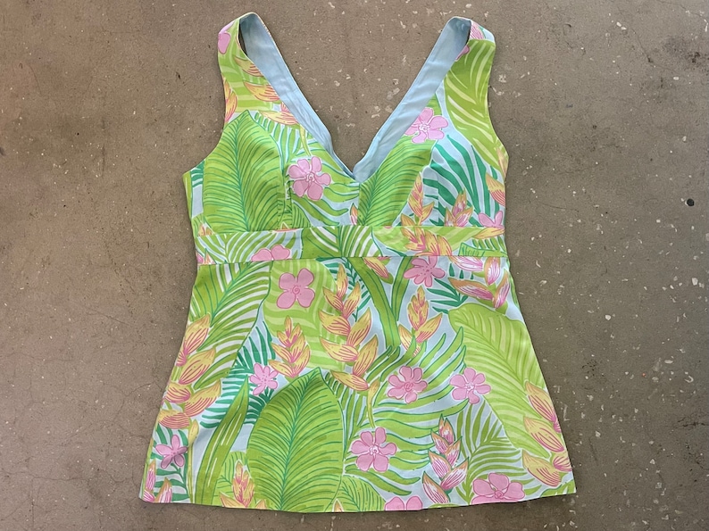 May include: A sleeveless, light blue and green top with a tropical print featuring pink flowers and green leaves.