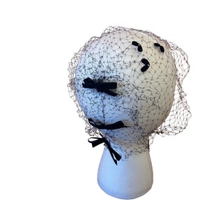 May include: A black bridal veil with a net design and black velvet bows. The veil is on a white mannequin head.