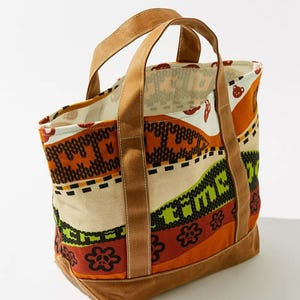 May include: A canvas tote bag with a colorful patterned design. The bag features brown handles and a brown base. The pattern includes orange, green, and cream colors with floral and geometric shapes.