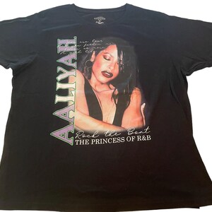 May include: Black t-shirt with a purple and green graphic of singer Aaliyah. The graphic includes a portrait of Aaliyah and the text "Rock the Boat The Princess of R&B".