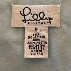 May include: A white tag with black text that reads "Lilly Pulitzer" and "SELF: 100% COTTON LINING: 65% POLYESTER 35% COTTON RN#88189 MADE IN VIETNAM". The tag also has a number "6" printed on it.