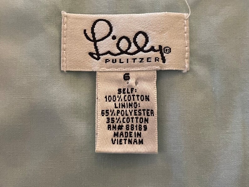 May include: A white tag with black text that reads "Lilly Pulitzer" and "SELF: 100% COTTON LINING: 65% POLYESTER 35% COTTON RN#88189 MADE IN VIETNAM". The tag also has a number "6" printed on it.