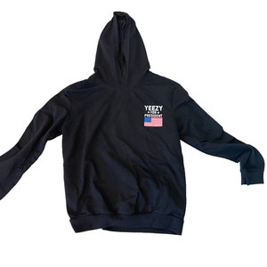 May include: Black hooded sweatshirt with the text "YEEZY FOR PRESIDENT" and an American flag graphic.