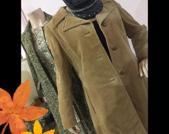 May include: A long, brown corduroy jacket with a button closure and a pointed collar. The jacket has a slightly fitted silhouette and is worn on a mannequin with a black leather cap.