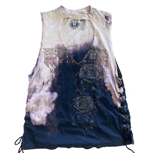May include: Sleeveless tank top with a keyhole neckline. The top features a tie-dye effect with a dark blue and cream color scheme. The front has a graphic with roses and the text "WORLD TOUR 1973". The sides have black lacing.